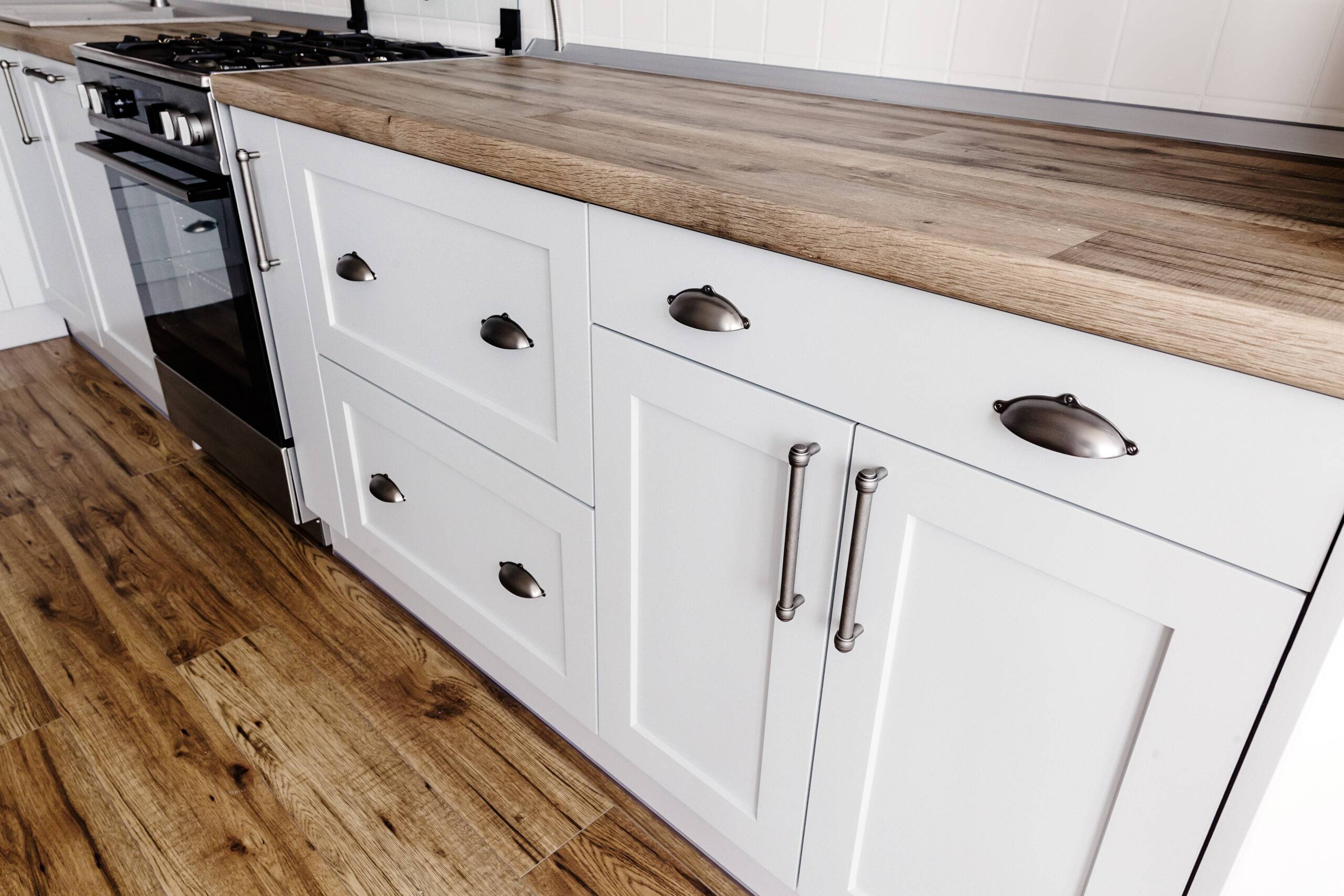 close-up steel handles on modern stylish light grey kitchen interior with furniture and stainless steel appliances in a new house. wooden countertop, steel stove, hardwood floor