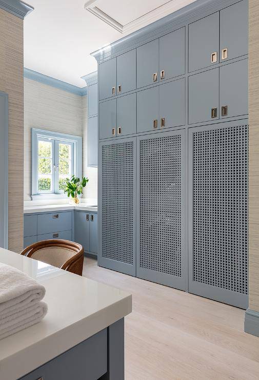 A stacked washer and dryer are hidden behind blue lattice doors located under stacked blue upper cabinets in a beautiful blue laundry room.