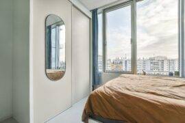 A bedroom in a high rise apartment, a mirror on the wall reflecting the view from the large window next to the bed.