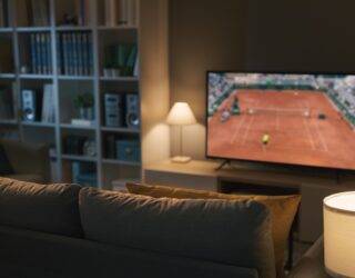 A couch facing a TV that's playing a tennis game.