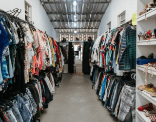 A photo of a long thrift store with clothing racks on either wall.